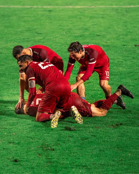 Joueurs en rouge célébrant un but à même la pelouse