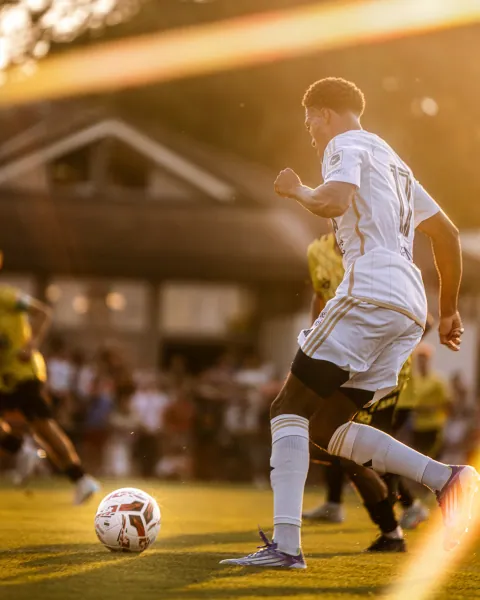 Joueur en blanc conduisant le ballon dans la lumière du soir