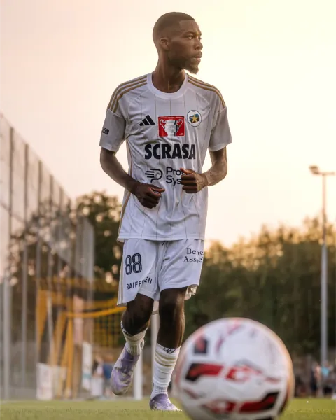 Attaquant en maillot blanc marchant vers le ballon au crépuscule