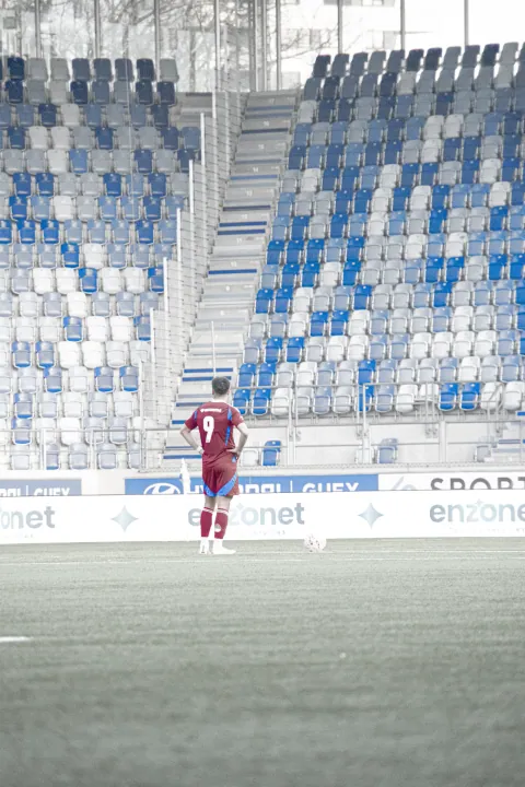 Joueur isolé devant les tribunes bleues du stade