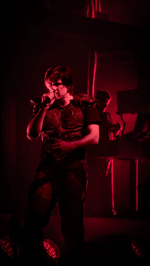 Orelsan micro en main sous une lumière rouge intense, musicien en arrière-plan