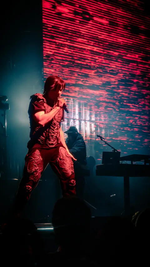 Orelsan en plein mouvement devant un écran géant strié de rouge à l'Arena de Genève