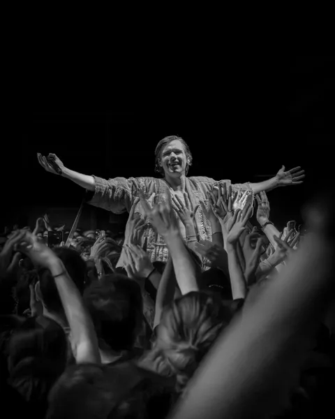 Orelsan bras ouverts porté par les mains du public, photo noir et blanc