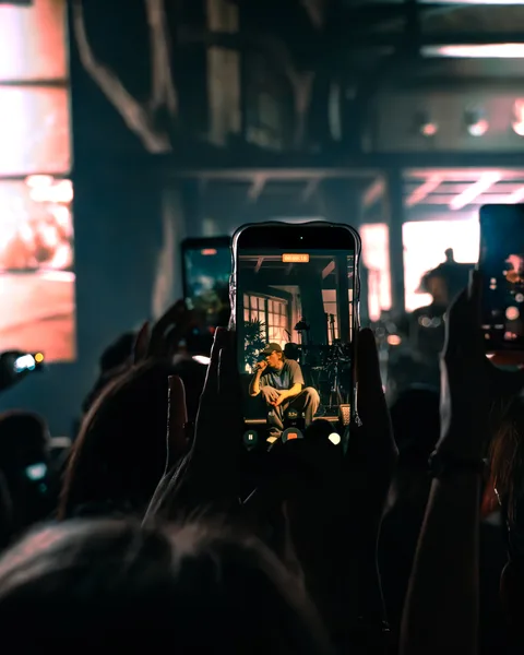 Écran de smartphone filmant Orelsan assis sur scène au milieu du public