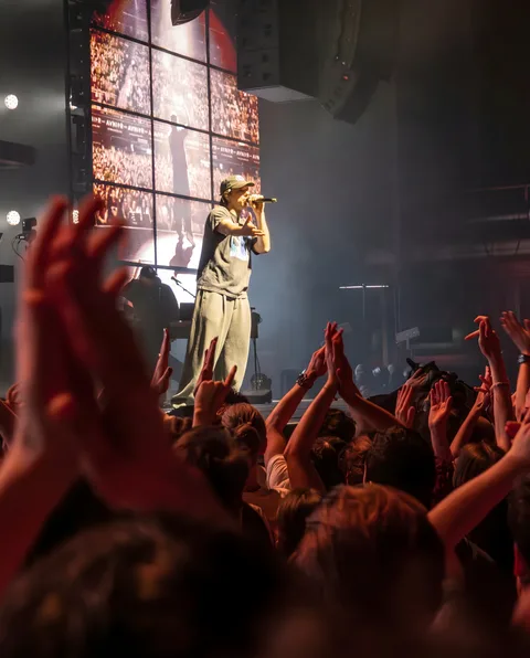 Orelsan casquette et micro en main face à la foule aux bras levés