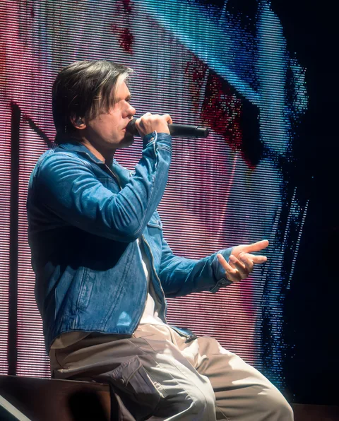 Orelsan de profil micro en main devant un écran aux couleurs saturées