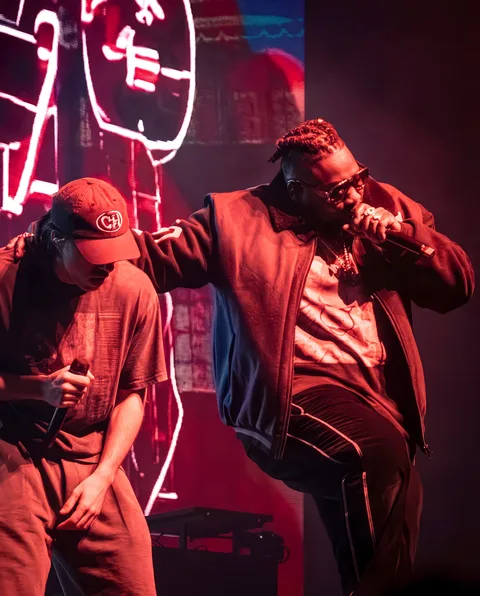 Deux rappeurs partagent la scène devant un décor néon lors du concert à Genève