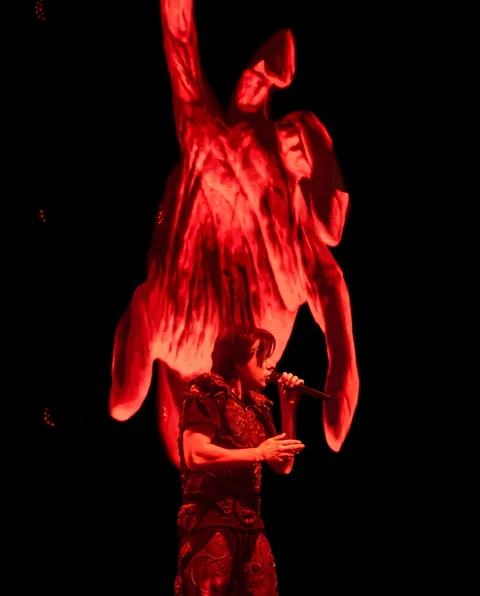 Orelsan chante en rouge devant une statue géante projetée sur fond noir